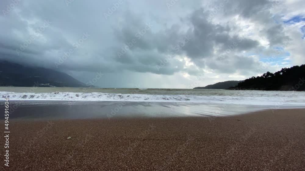View from the sandy beach to overcast seascape. Foam waves are raging and washing the coast, but sun and blue sky are already visible among clouds after storm View from the sandy beach to overcast seascape. Foam waves are raging and washing the coast, but sun and blue sky are already visible among clouds after storm