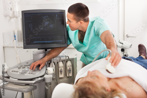 Young male doctor using ultrasound scan examining female patient in the modern hospital