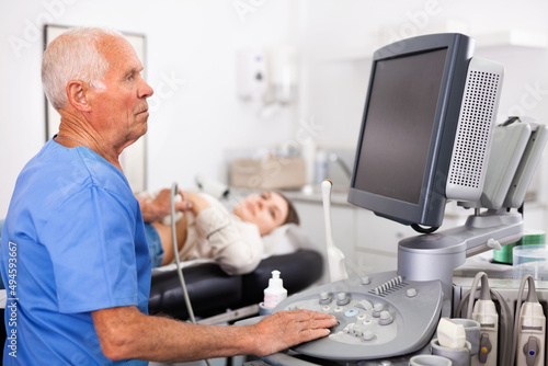 Elderly positive man sonographer using ultrasonography machine checking female patient in hospital diagnostic room