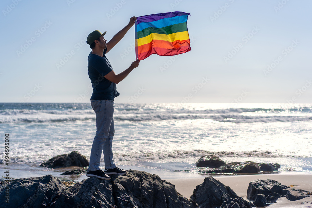person holding rainbow flag, LGTBQ, against wind on the beach