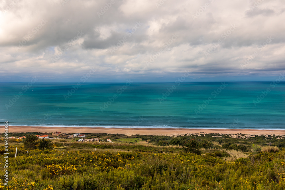 Beautiful beach of Salgados with the village of Nazare in the background, Portugal. Beautiful beach with turquoise waters in a cloudy day Beautiful beach of Salgados with the village of Nazare in the background, Portugal. Beautiful beach with turquoise waters in a cloudy day