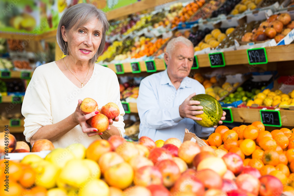 European old man and woman choosing fresh fruits in greengrocer.