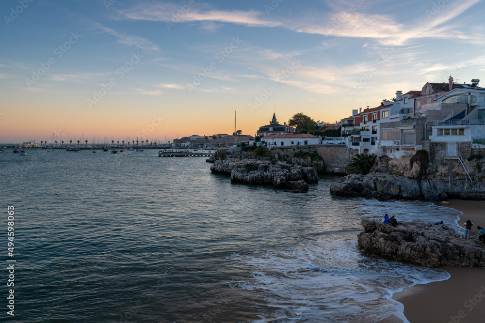 Rainha beach in Cascais at sunset with sail boats on the sea and houses on the coast, in Portugal