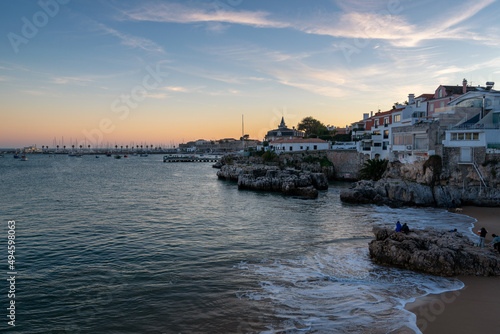 Rainha beach in Cascais at sunset with sail boats on the sea and houses on the coast, in Portugal