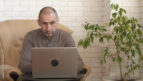 Man make eyes relaxation at home. An overworker man makes eyes massage by the notebook in the room. photo