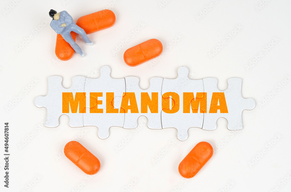 On the white surface of the tablet, a miniature human figure and puzzles with the inscription - MELANOMA On the white surface of the tablet, a miniature human figure and puzzles with the inscription - MELANOMA