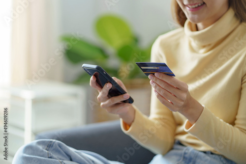Young woman using smartphone and credit card for online shopping at home.