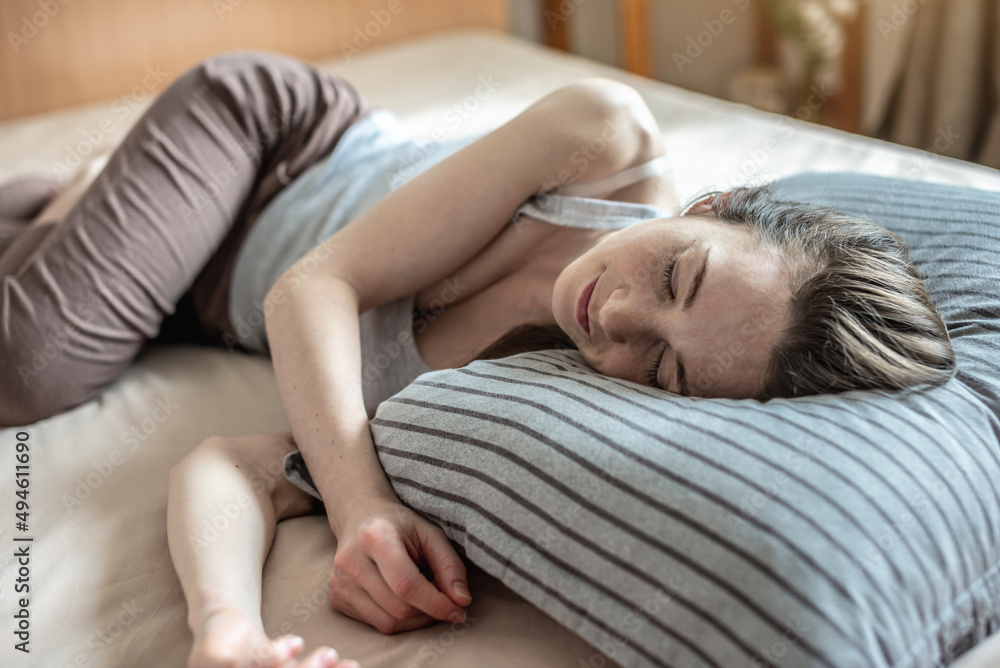 Young happy woman is lying in bed in the morning with her eyes closed and waking up. Concept of healthy sleep, comfort and a pleasant start of new day Young happy woman is lying in bed in the morning with her eyes closed and waking up. Concept of healthy sleep, comfort and a pleasant start of new day