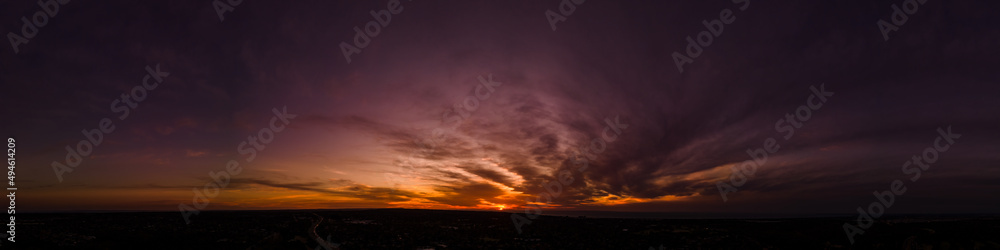 Dark wispy clouds in a deep purple sky at the end of a glowing orange sunset aerial panoramic Dark wispy clouds in a deep purple sky at the end of a glowing orange sunset aerial panoramic