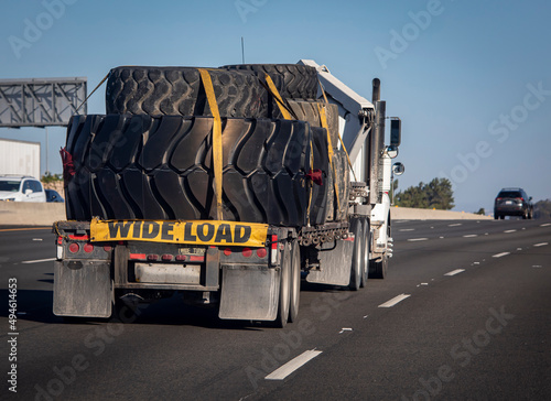 Heavy equipment tires being hauled on a flatbed trailer with a wide load sign