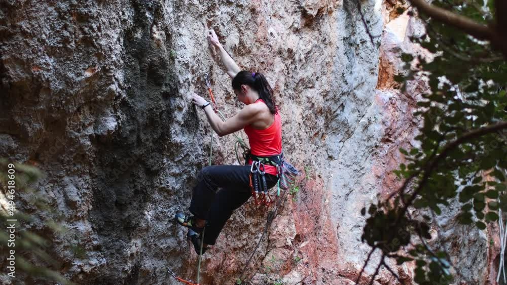 A woman climbs the rock. Training on natural terrain. Extreme sport. The climber trains on a natural relief. A young woman with a rope goes in for the sport of rock climbing on a rock. A woman climbs the rock. Training on natural terrain. Extreme sport. The climber trains on a natural relief. A young woman with a rope goes in for the sport of rock climbing on a rock.