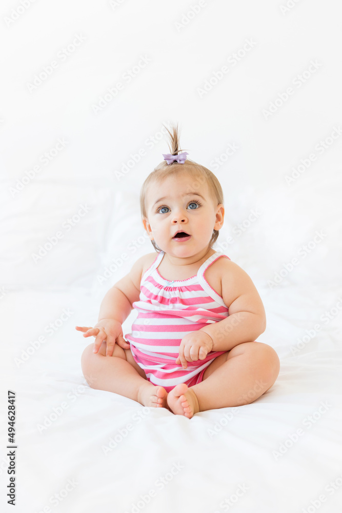 Cute chubby baby girl sitting on white bed Cute chubby baby girl sitting on white bed