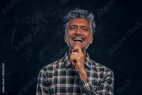 Glad elderly man dressed in plaid shirt against dark background