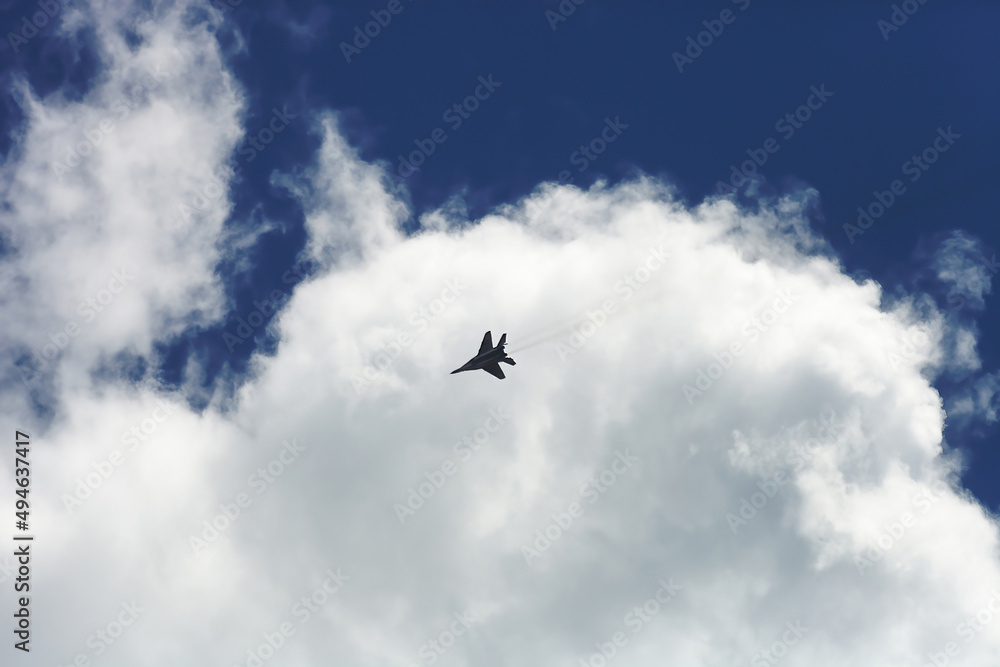 Fast Fighter flying high in blue sky background. Super sonic airplane silhouette flight in clouds
