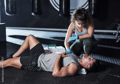 The journey to health just got a bit more tough. Shot of a masked young woman giving an injured man first aid at the gym. photo