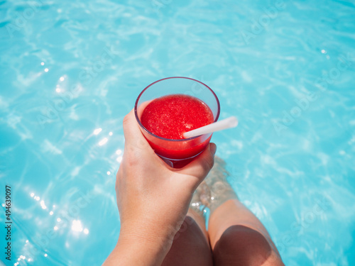 Beautiful glass with a refresh strawberry smoothie and a pretty woman on the background of the swim pool. Top view, close-up. Vacation and travel concept. Moments of celebration