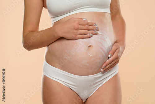 Cropped view of pregnant woman applying cosmetic cream on her belly to avoid stretch marks photo
