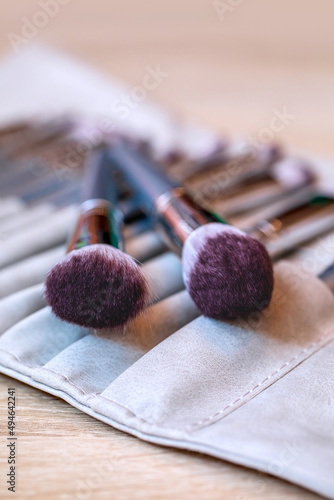 A set of large assorted makeup brushes are packed in a leather case on the make-up artist's desk. Vertical photo layout of cosmetic accessories. Materials for creating beauty.
