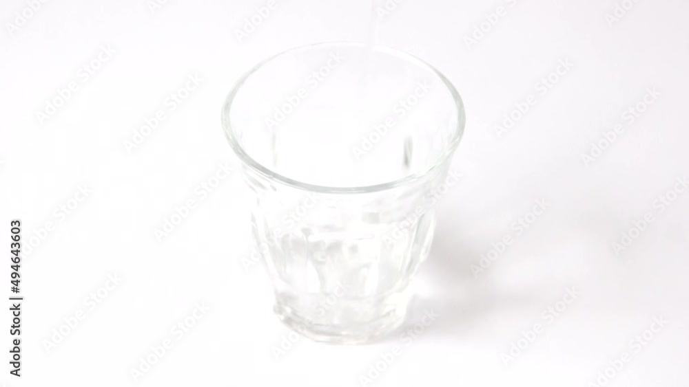 透明なグラスにそそがれる飲料水。白いテーブルの上にシンプルなコップが置かれている。 透明なグラスにそそがれる飲料水。白いテーブルの上にシンプルなコップが置かれている。