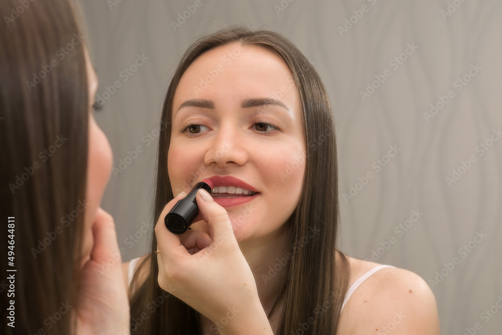 The girl at the mirror puts makeup on young and healthy skin. The girl at the mirror puts makeup on young and healthy skin.