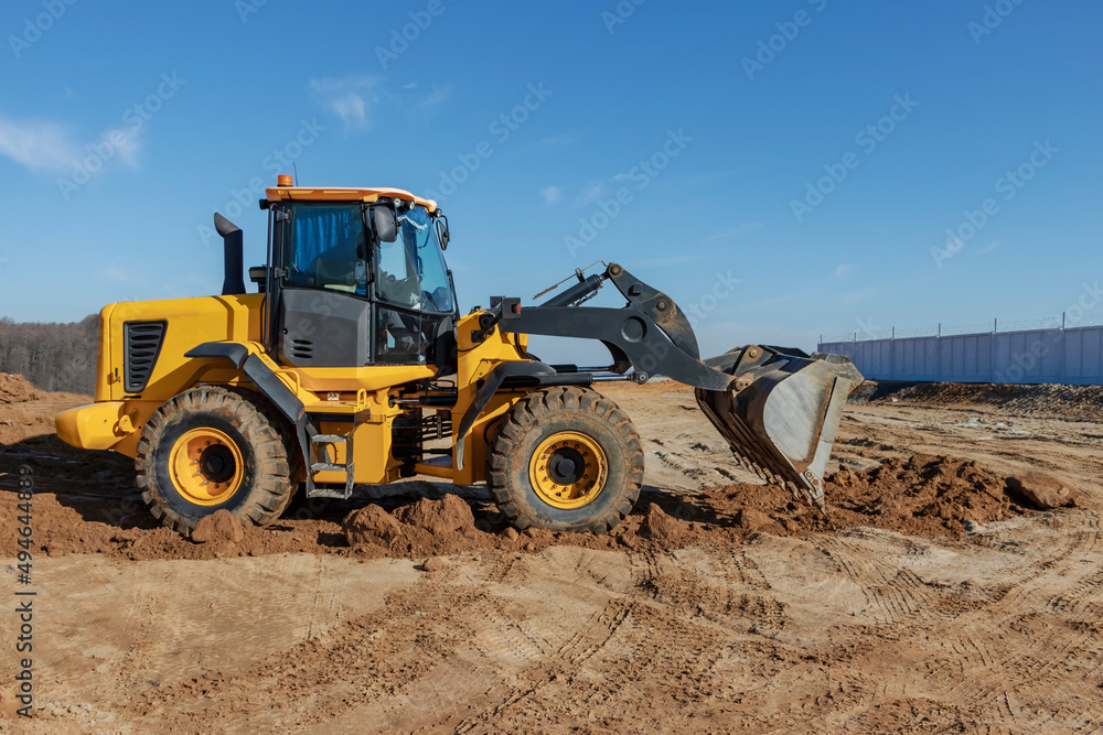 Bulldozer or loader moves the earth at the construction site against the blue sky. An earthmoving machine is leveling the site. Construction heavy equipment for earthworks. Bulldozer or loader moves the earth at the construction site against the blue sky. An earthmoving machine is leveling the site. Construction heavy equipment for earthworks.