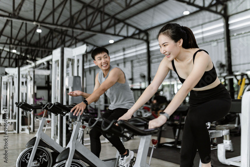 exercise concept The well-shaped lady and the muscular man being entertaining having small chat while riding the exercise bike machines © Pichsakul