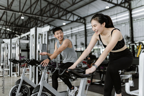 exercise concept The well-shaped lady and the muscular man being entertaining having small chat while riding the exercise bike machines