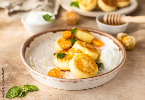 Curd or ricotta fritters with physalis, honey, yogurt and mint on a ceramic plate. Cottage cheese pancakes or syrniki. Healthy and tasty breakfast.