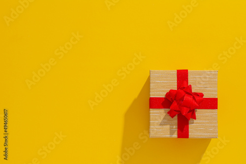 One grey gift box with Red sparkle ribbon and bow on yellow table background. Minimal festive gift background. Top view. Flat lay.	