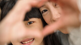 closeup with selective focus asian girl and mother showing love sign with hands. they look through fingers with smiles