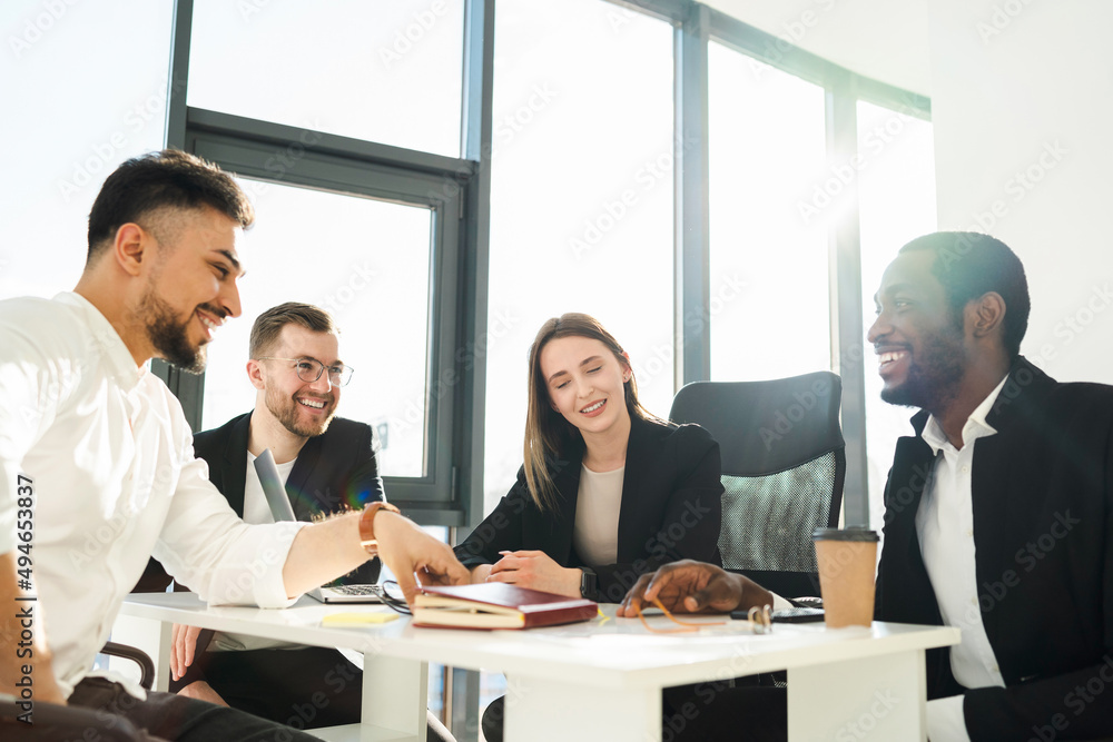 Group of multiracial company workers in formal wear having a meeting in a sunny office Group of multiracial company workers in formal wear having a meeting in a sunny office