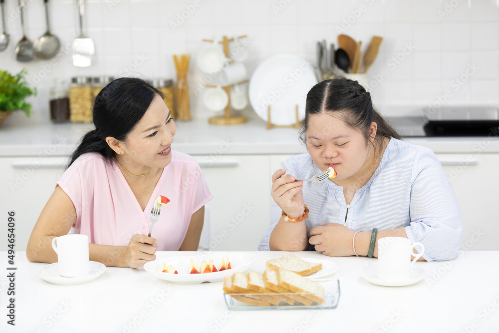 mother with down syndrome teenage girl or her daughter, eating apple together in a kitchen