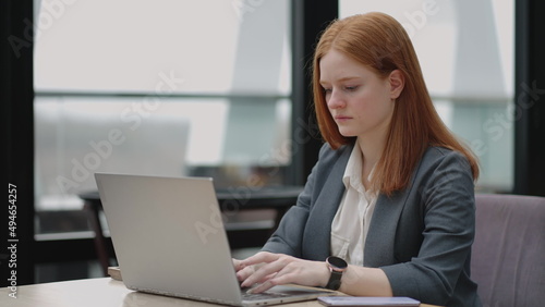 woman is working with laptop in office, typing e-mail for partners and employees, serious and successful businesswoman