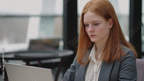 young businesswoman in grey jacket is working with notebook in cafe or restaurant, checking emails and reports
