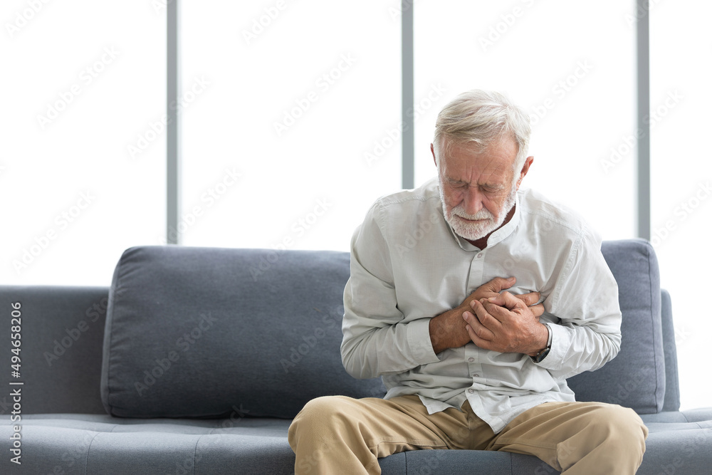 senior elderly man chest pain or suffering from heart attack on a sofa