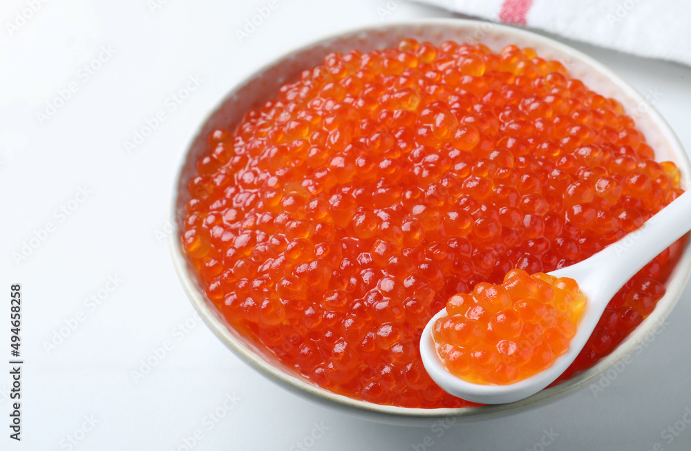 Bowl and spoon with delicious red caviar on white table, closeup Bowl and spoon with delicious red caviar on white table, closeup