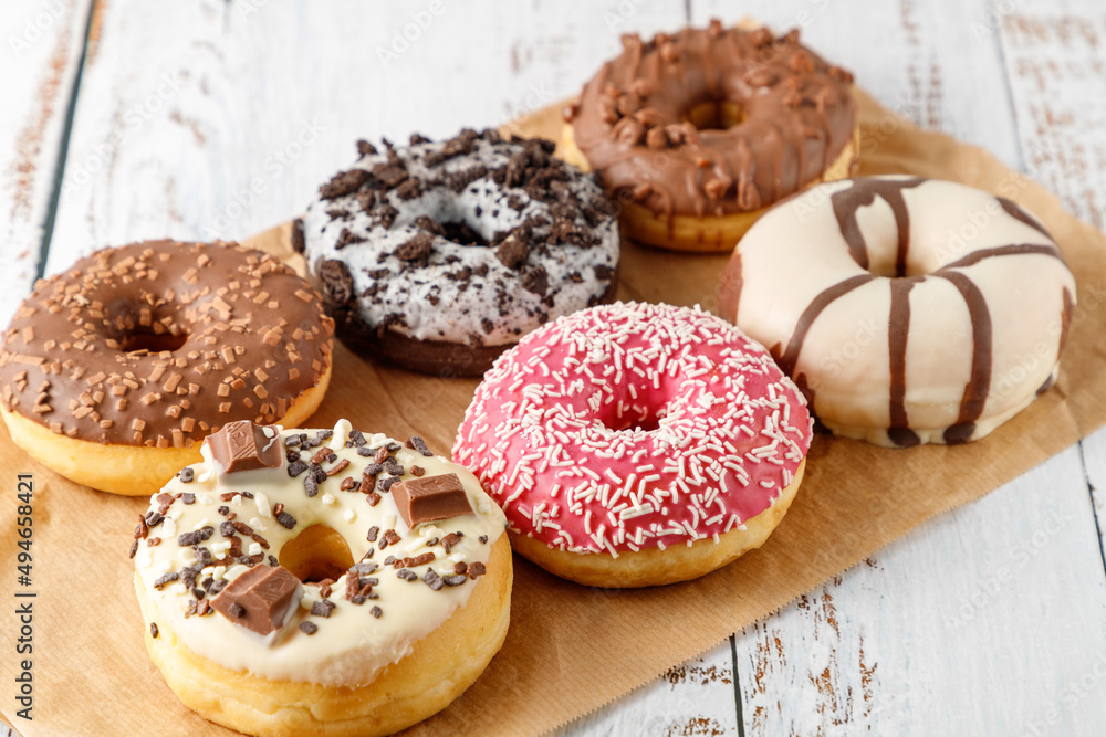 Set of assorted colorful white and dark chocolate glazed donuts with mixed sprinkles on paper on wooden table.