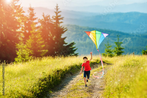 Little happy child boy running with kite. Wonderful mountain landscape in Alps at sunset.