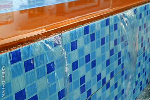 Closeup overflowing water of golden brown and vibrant blue tiled swimming pool spillway photo