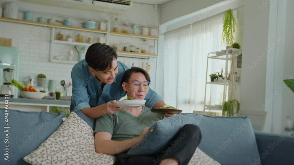 Young smiling gay couple having healthy food in the living room at home, LGBTQ and diversity concept. Young smiling gay couple having healthy food in the living room at home, LGBTQ and diversity concept.