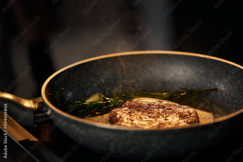 Close up view of preparation appetizing beef burger on grill with copy space. Frying and smoking juicy beef in pan with garlic and rosemary stick in restaurant kitchen . Concept of food.
