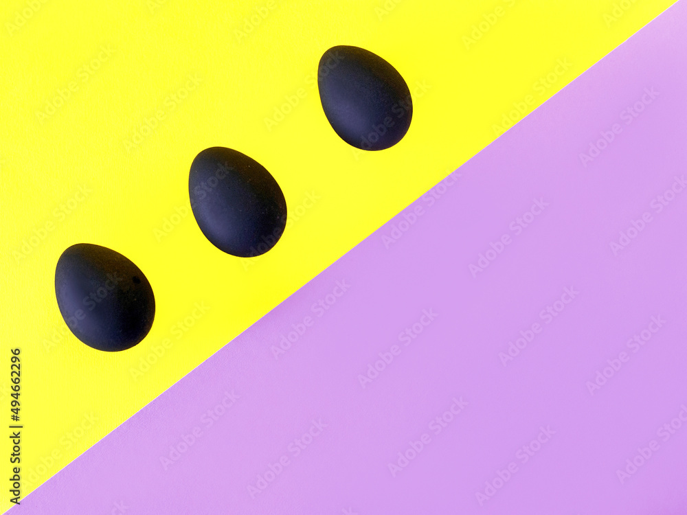 Black eggs on the yellow and violet background. Easter, diversity, geometric, pattern, food concept Black eggs on the yellow and violet background. Easter, diversity, geometric, pattern, food concept