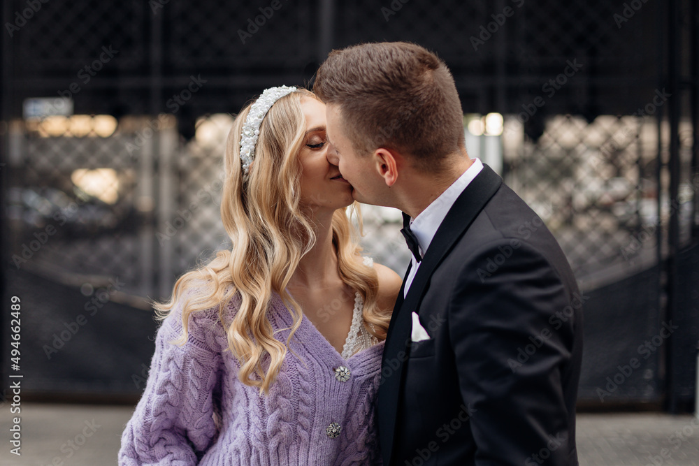 Beautiful couple of bride with long wavy fair hair in bridal dress, lilac cardigan with bandeau on head and bridegroom.