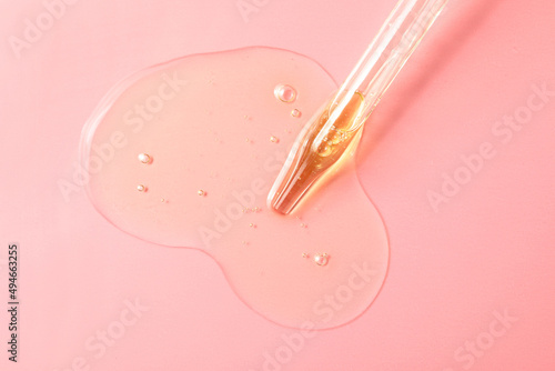 Dripping hydrophilic oil from pipette on pink background, top view photo