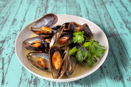 Mussels cooked with an Italian recipe called tarantina mussels in white, in a plate with parsley on rustic blue wooden table photo