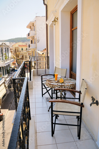 A small metal table with chairs on the beautiful balcony. Orange juice in a tall transparent glass on an old metal table with beautiful patterns. Next to it is a fresh orange cut in half.
