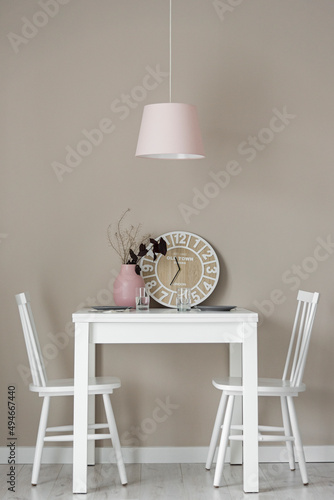 Jadalnia w kolorach beżowych, białych i różowych. Firanka i zasłony.  Stolik do jedzenia z wisząca różową lampą. Zegar i ozdoby