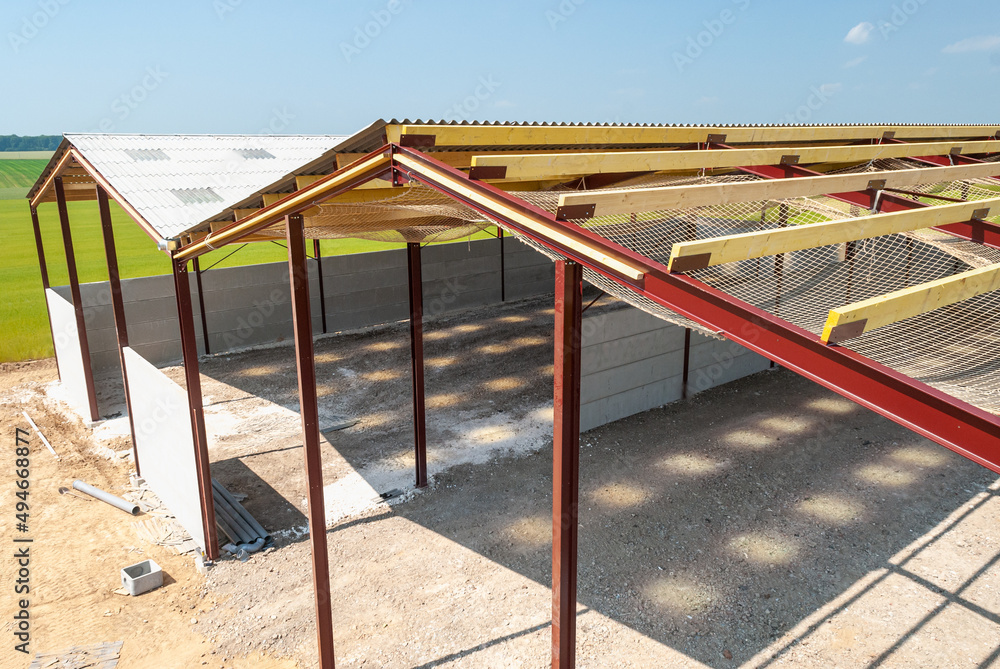 Construction d'un batiment agricole à ossature métallique. Pose de plaque fibres-ciment ondulée Eternit pour la toiture. Filets antichute