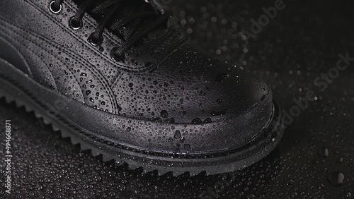Black male shoe and water drops on a black background close-up.