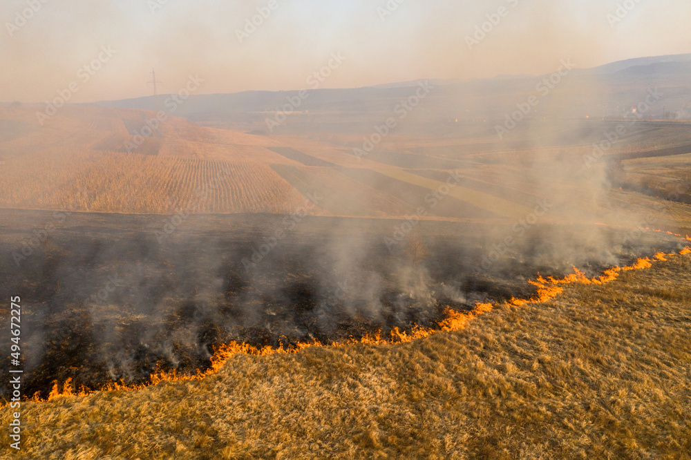 Aerial view of spring dry grass burning field. Fire and smoke in the meadow, nature pollution and danger,common waste are burned